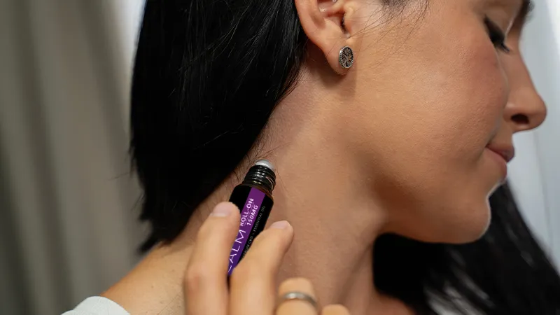 CBD Roll Ons | CBD Rollers | CBD Essential Oil Roll Ons by Broad Essentials A woman applying an essential oil roll on to her neck.